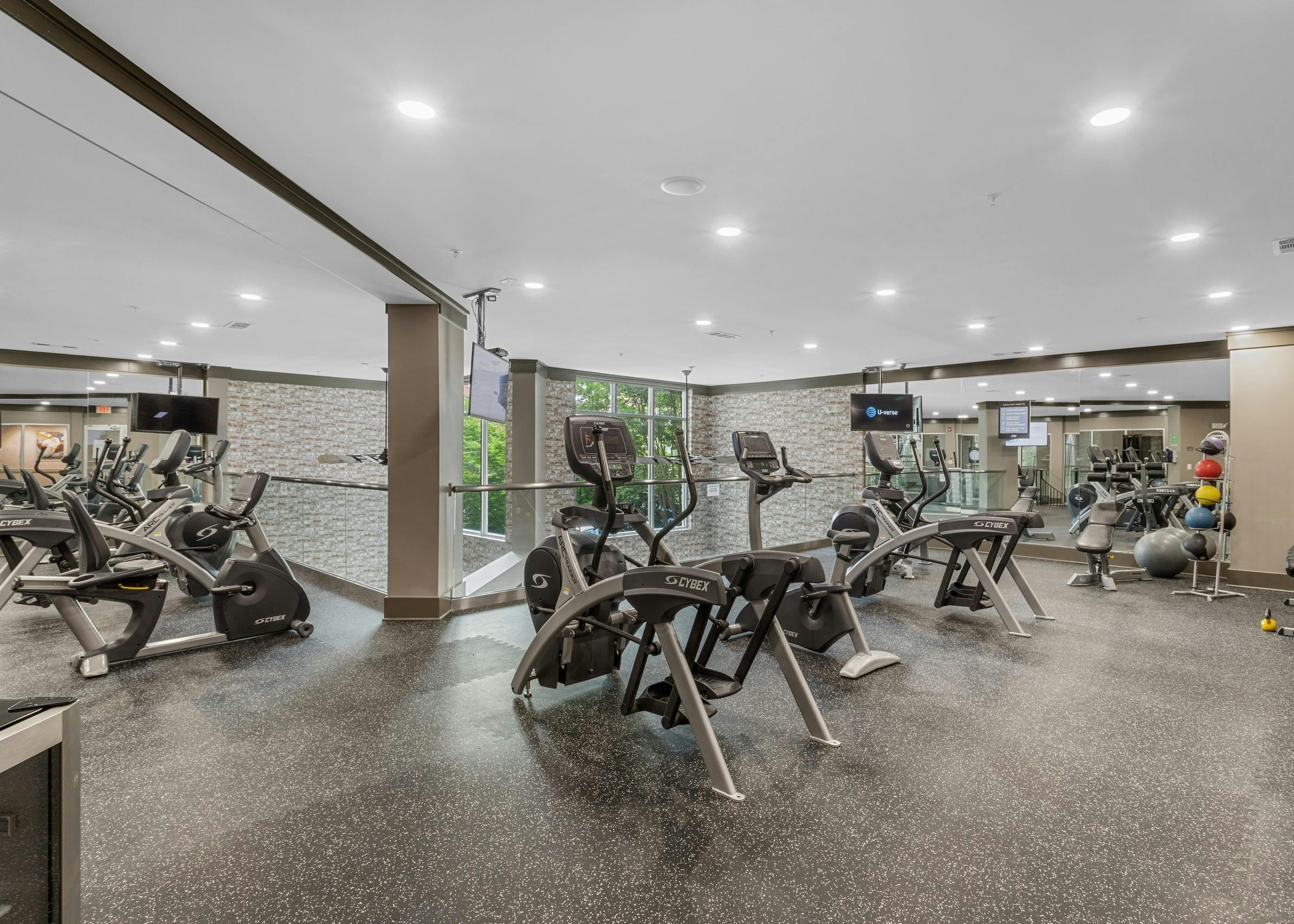 The fitness center at AMLI North Point with speckled floors and exercise equipment with hanging TVs and a full mirror wall