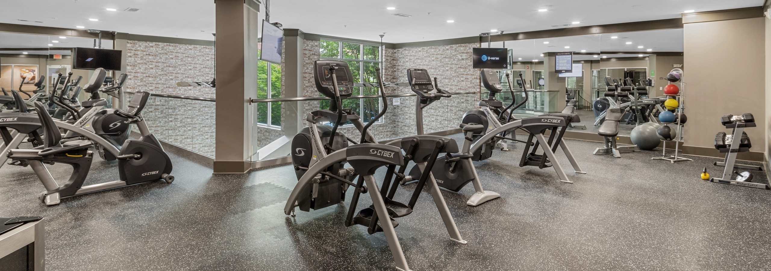 The fitness center at AMLI North Point with speckled floors and exercise equipment with hanging TVs and a full mirror wall