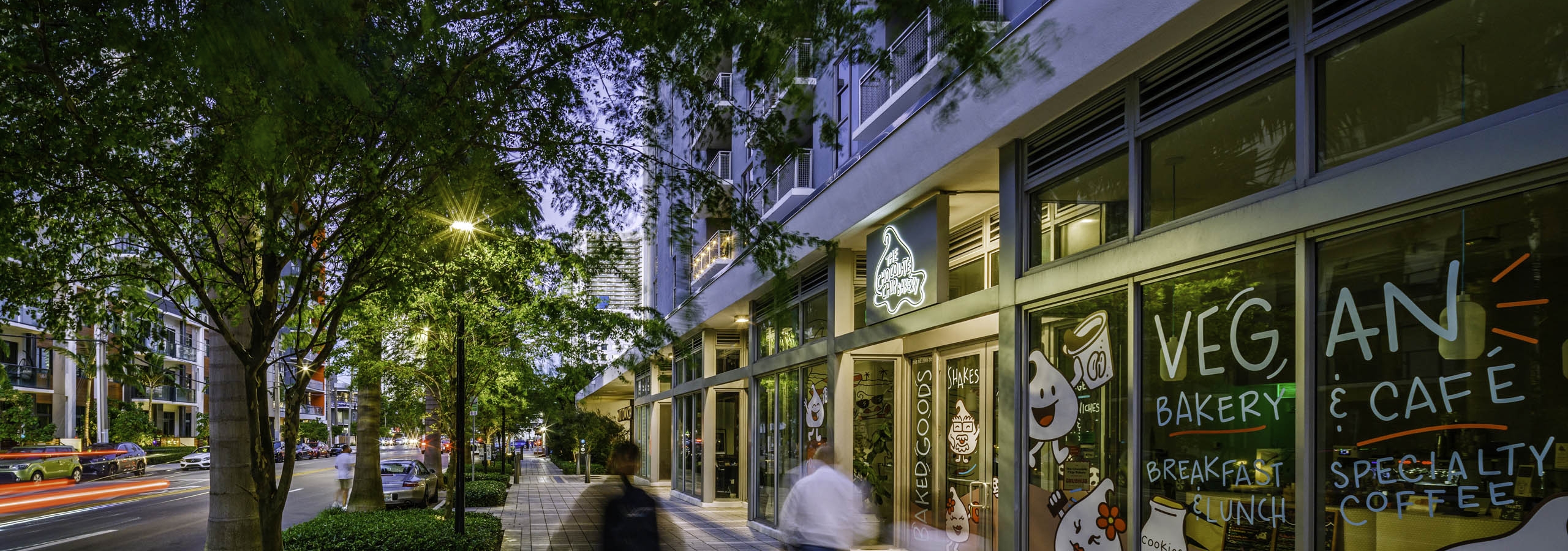 Sidewalk and streetscape view of retail bakery and cafe at AMLI Midtown 29 with people in motion and trees overhanging