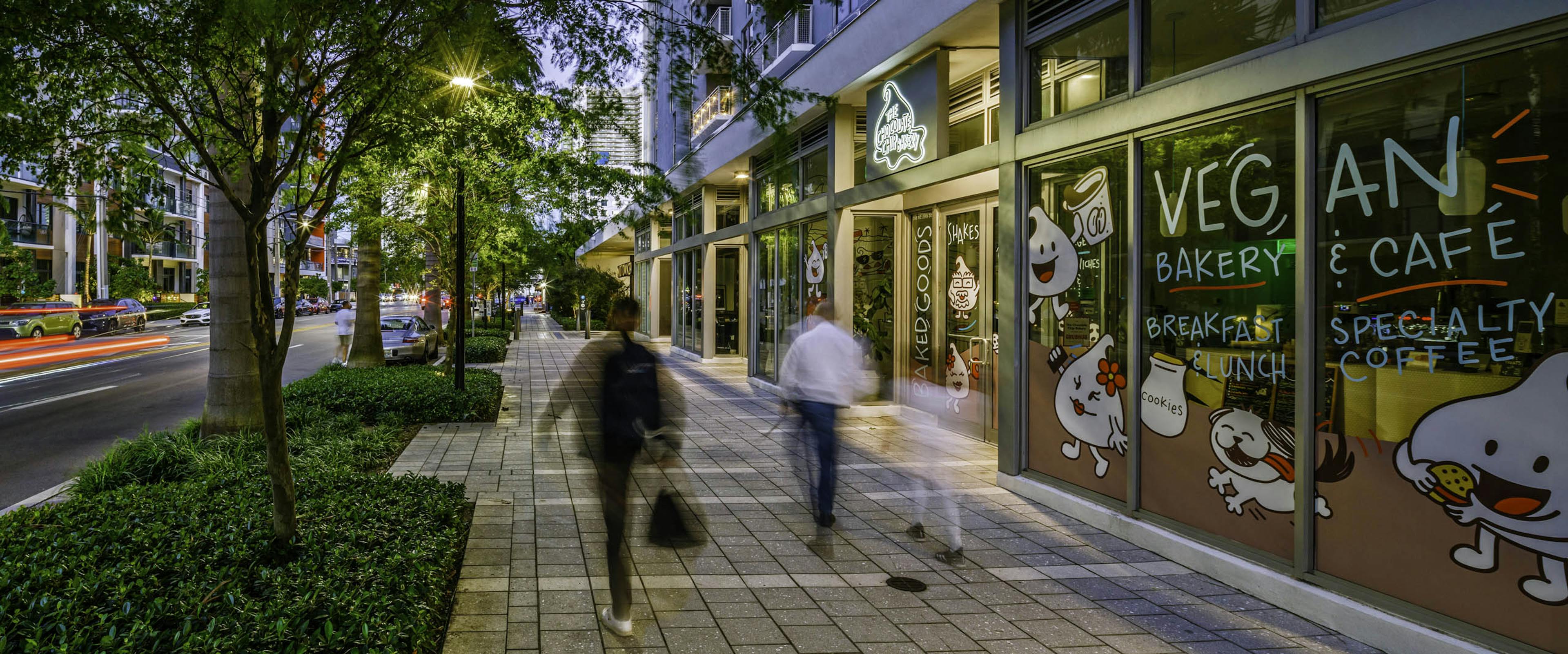 Sidewalk and streetscape view of retail bakery and cafe at AMLI Midtown 29 with people in motion and trees overhanging