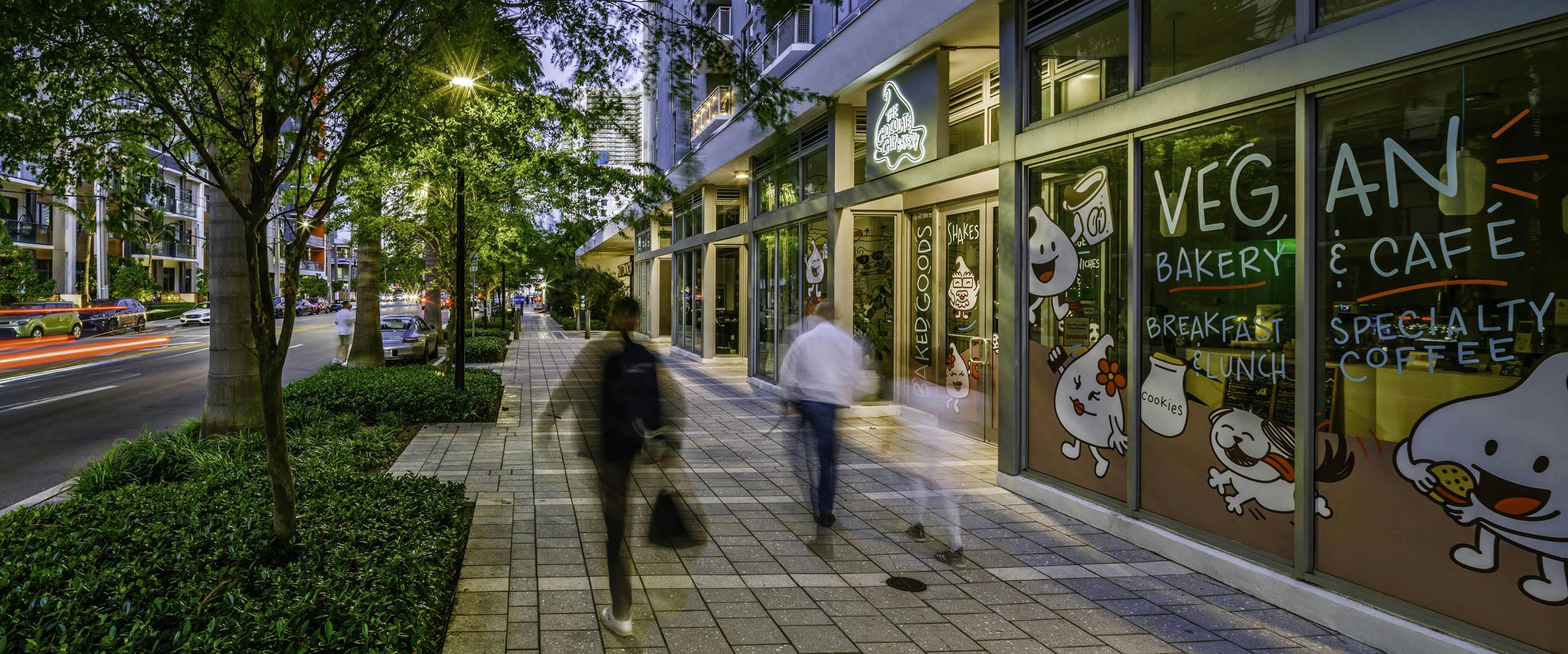 Sidewalk and streetscape view of retail bakery and cafe at AMLI Midtown 29 with people in motion and trees overhanging