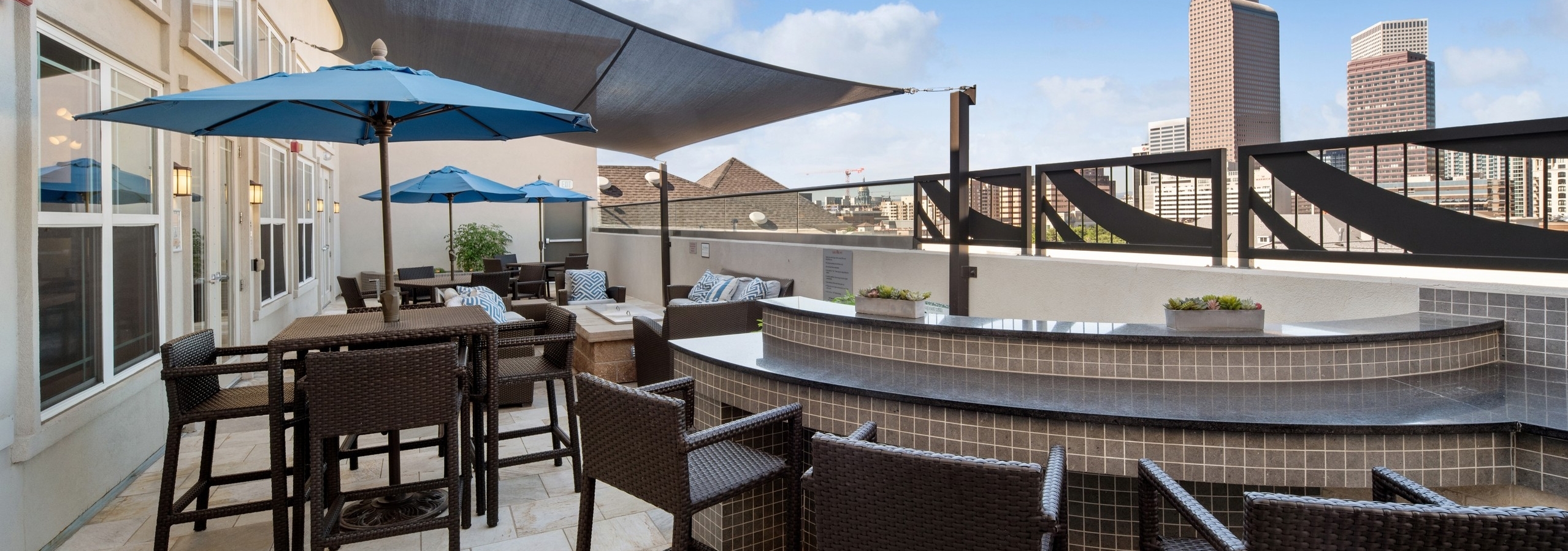 Exterior view of a rooftop lounge at AMLI Park Avenue with a bar seating area with chairs and tables with blue umbrellas