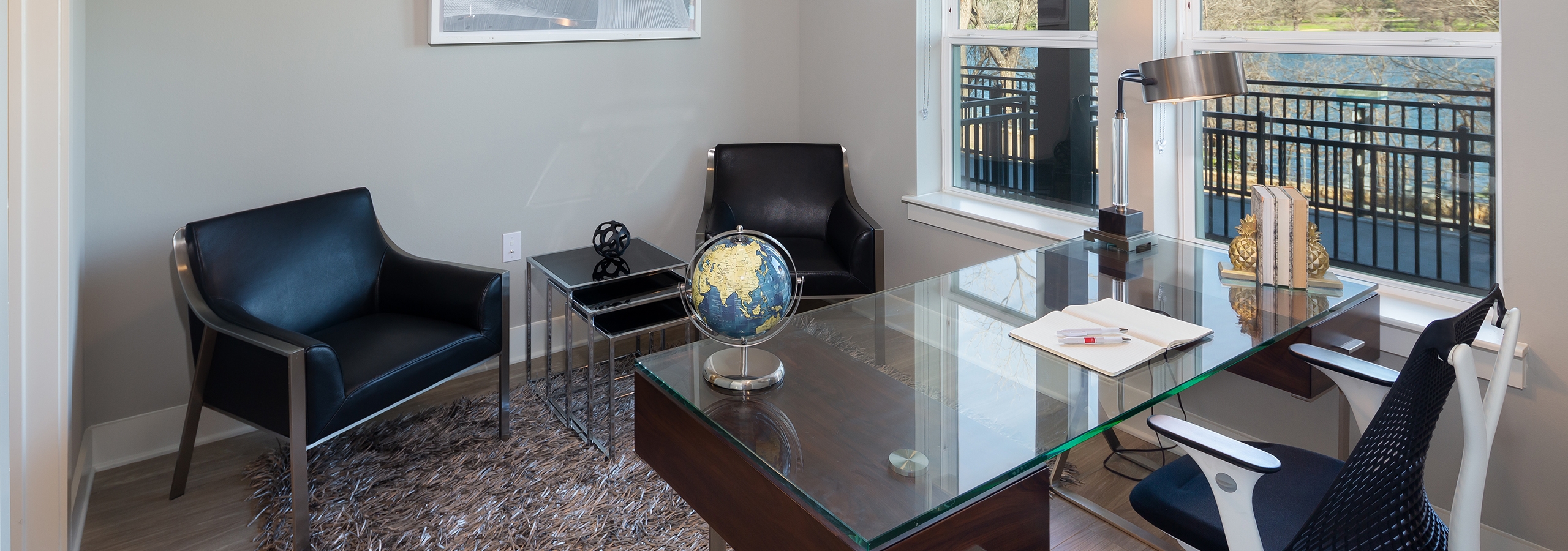 Interior of office at AMLI South Shore with a scenic window view and a large glass desk across from two leather chairs