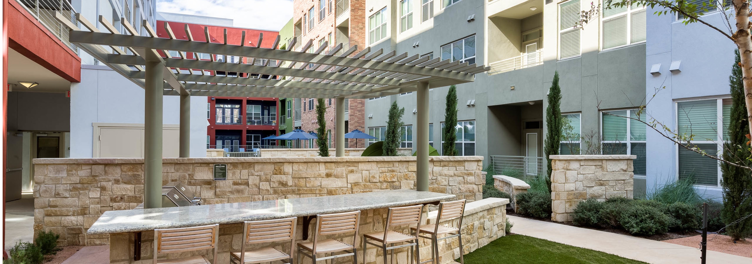Outdoor barbecue area at AMLI at Mueller with bar seating in front of a pergola with view of exterior building facade