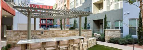 Outdoor barbecue area at AMLI at Mueller with bar seating in front of a pergola with view of exterior building facade