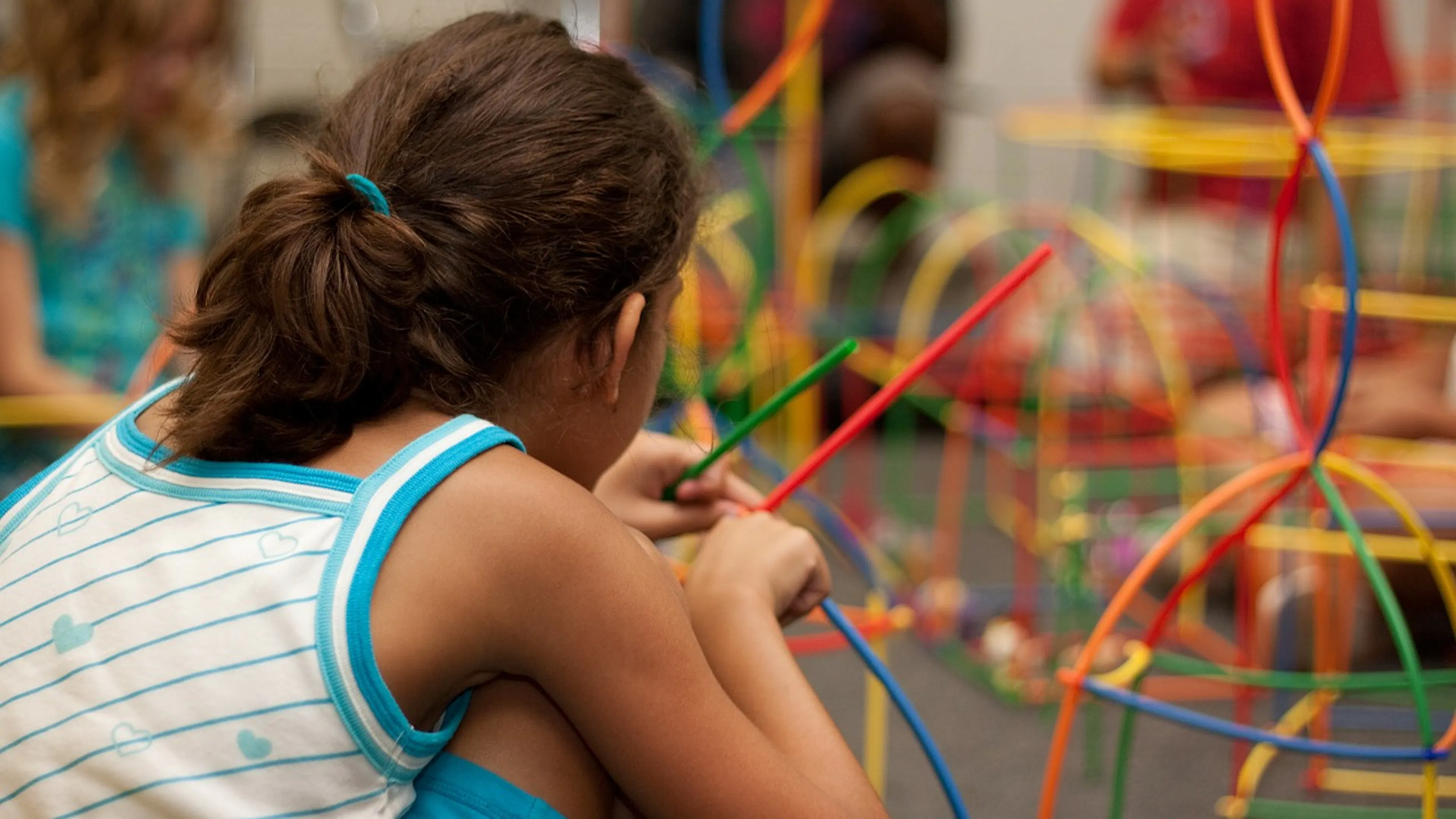 child facing away playing with straws and connector toys with more toys in the background