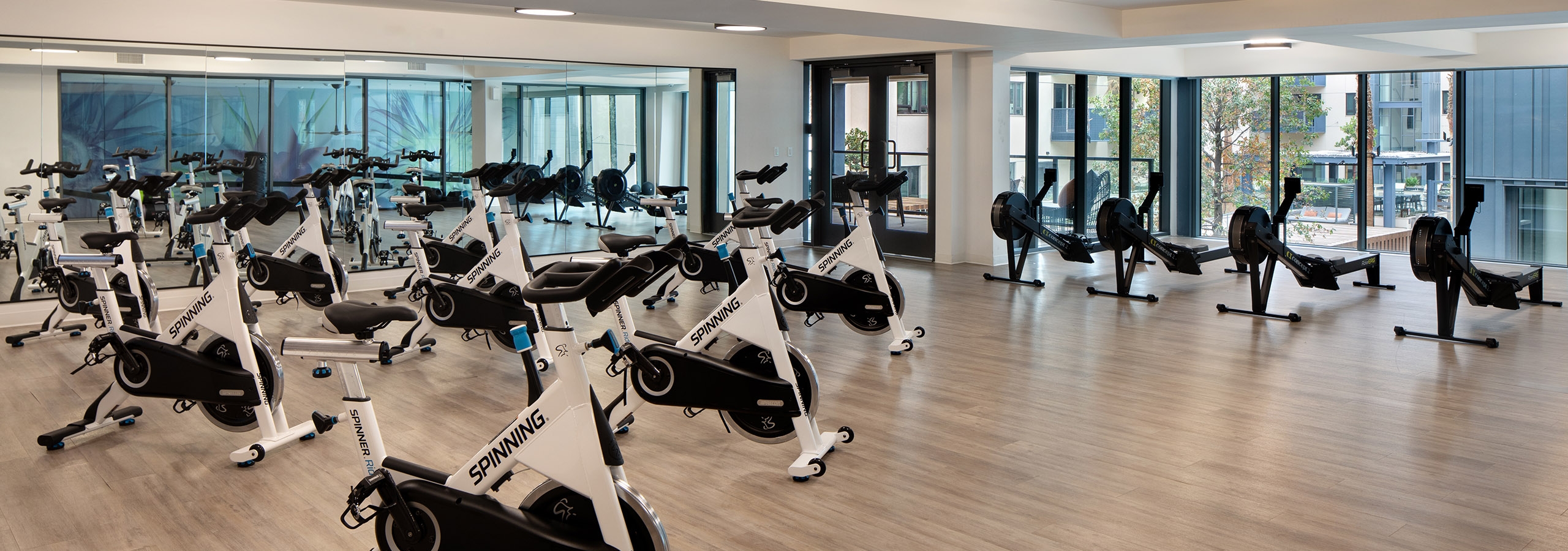 Upper level of fitness center at AMLI Old Pasadena apartments with spin bikes and row machines lined up facing the pool area