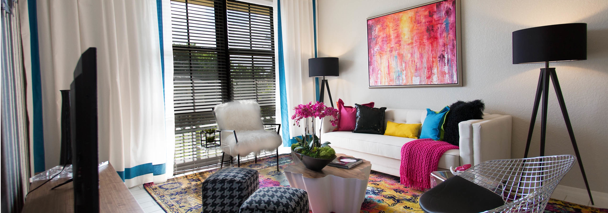 Interior of an AMLI Dadeland apartment living area with white sofa, pillows, modern colorful artwork and black floor lamps