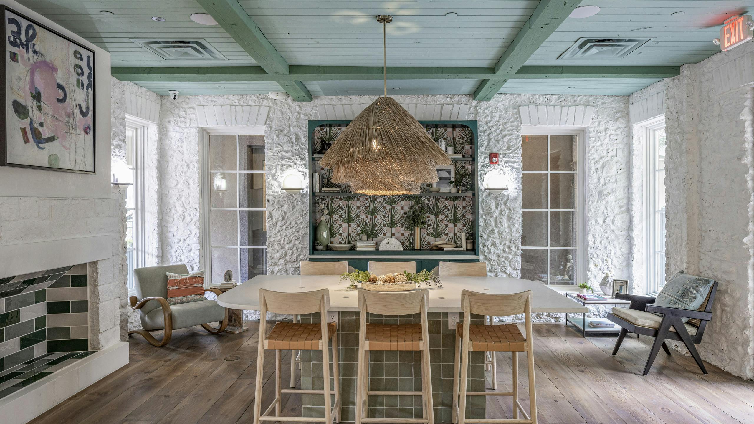 Interior view of AMLI 300 resident lounge with white table with 6 wooden chairs and white stone walls and green beamed ceiling