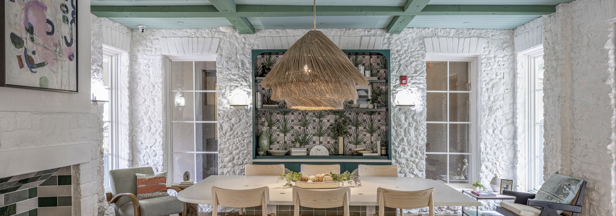 Interior view of AMLI 300 resident lounge with white table with 6 wooden chairs and white stone walls and green beamed ceiling