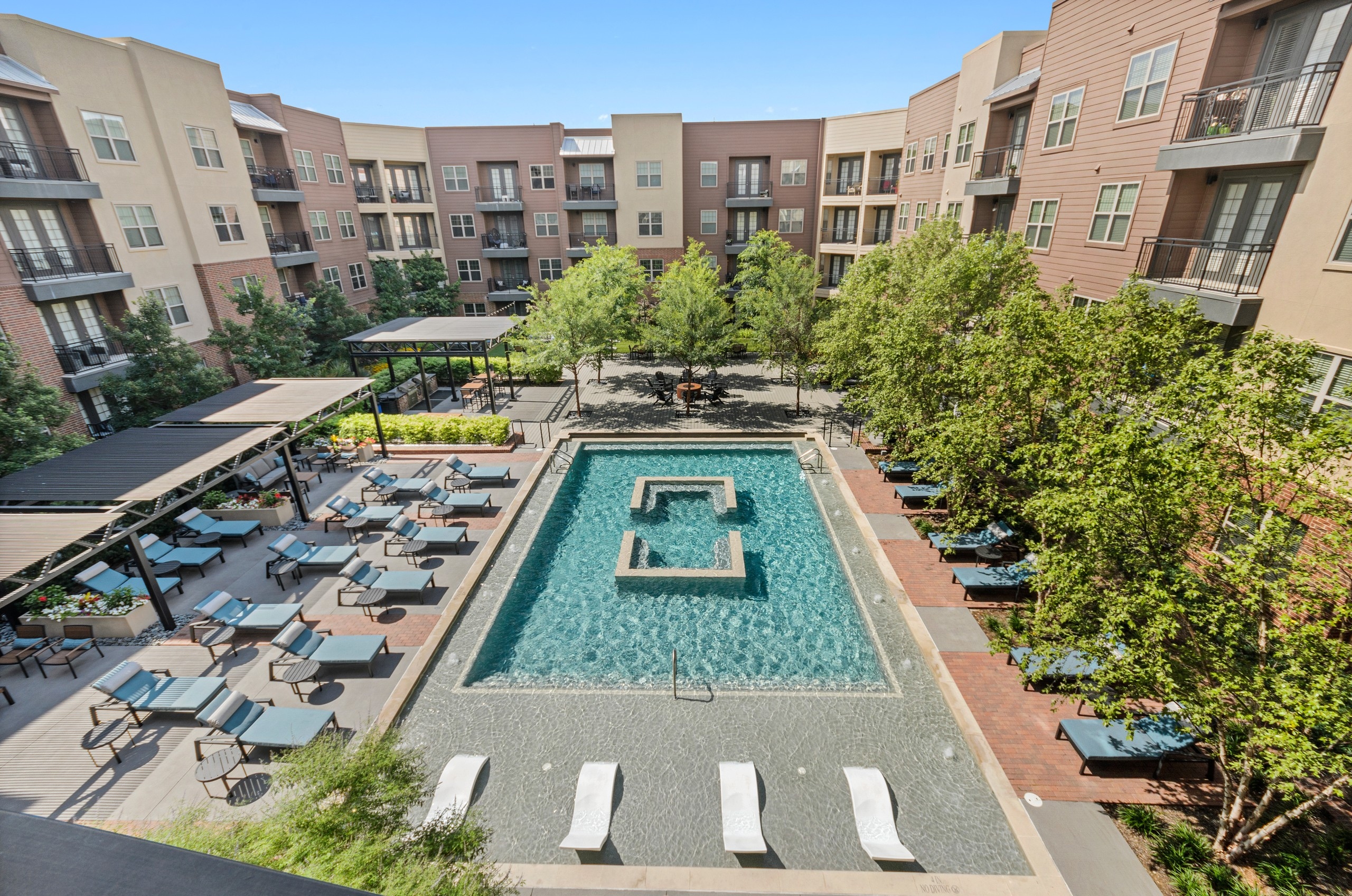 AMLI Grapevine apartments courtyard pool with blue lounge seating and surrounded by lush landscaping and tall trees
