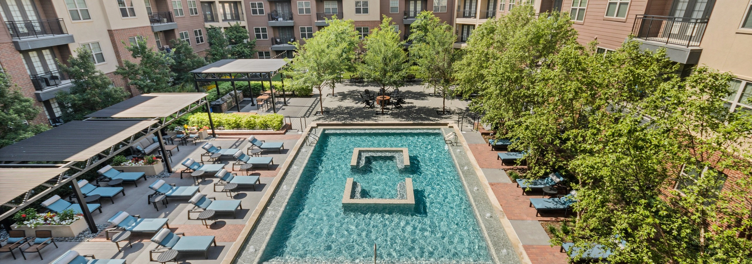 AMLI Grapevine apartments courtyard pool with blue lounge seating and surrounded by lush landscaping and tall trees