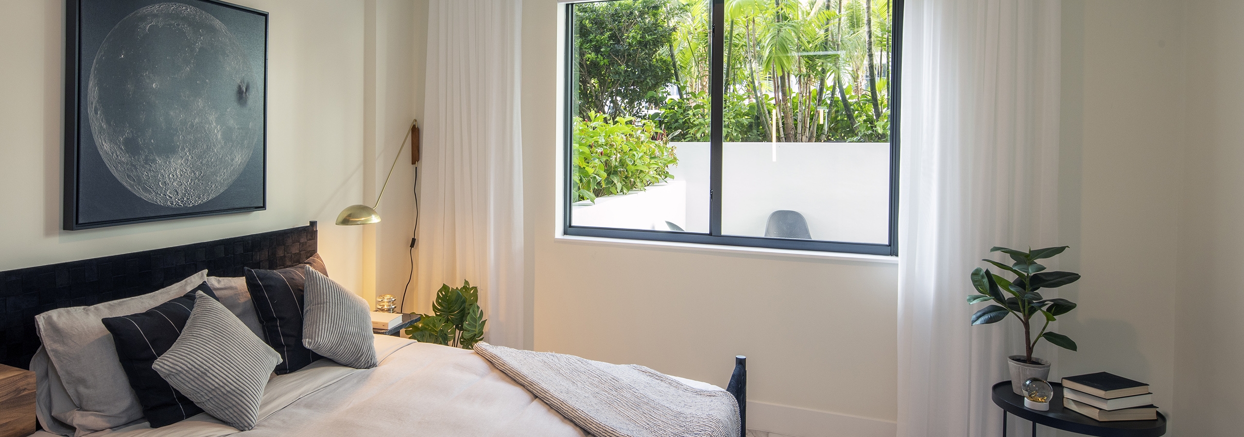 AMLI Midtown Miami apartment bedroom with window overlooking patio and bed and small table with plant and books