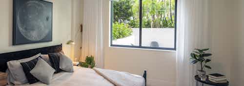 AMLI Midtown Miami apartment bedroom with window overlooking patio and bed and small table with plant and books