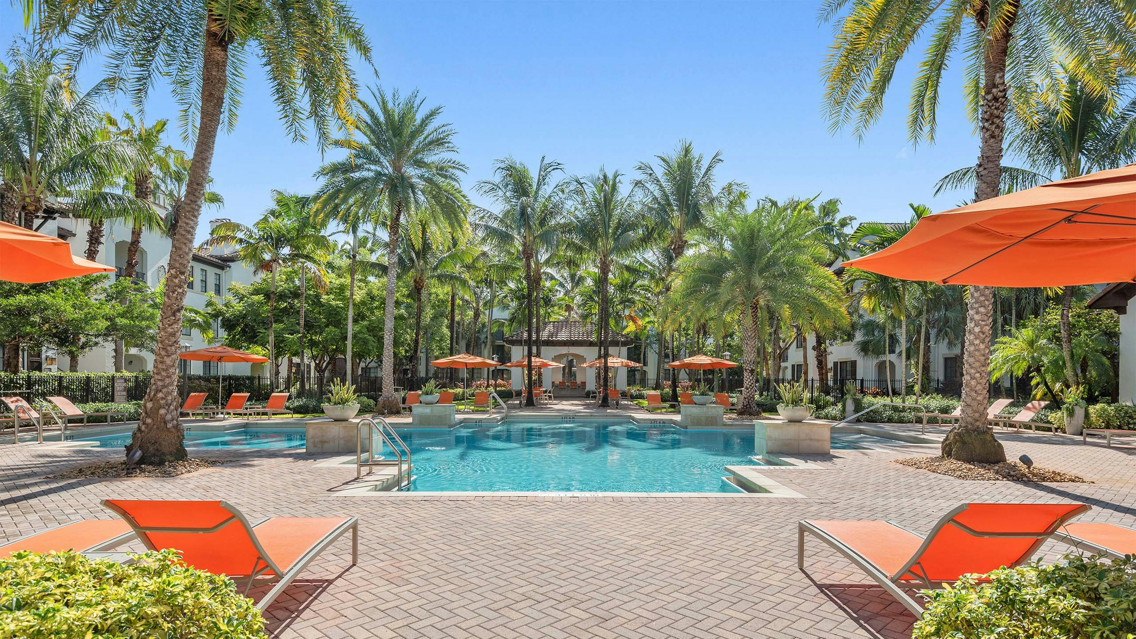 AMLI Toscana Place swimming pool with lush palm trees and orange lounge chairs and umbrellas with view of clubhouse
