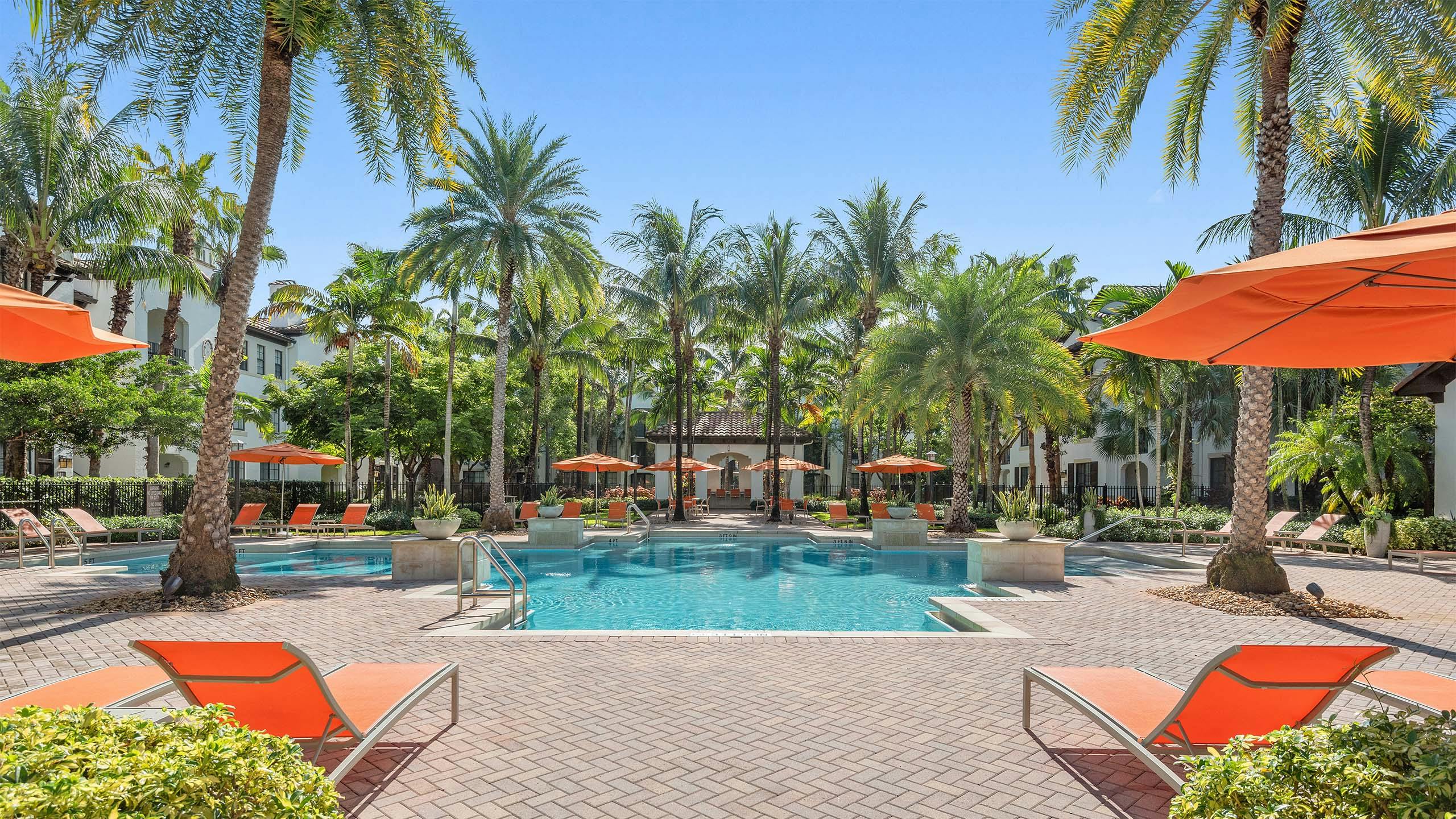 AMLI Toscana Place swimming pool with lush palm trees and orange lounge chairs and umbrellas with view of clubhouse