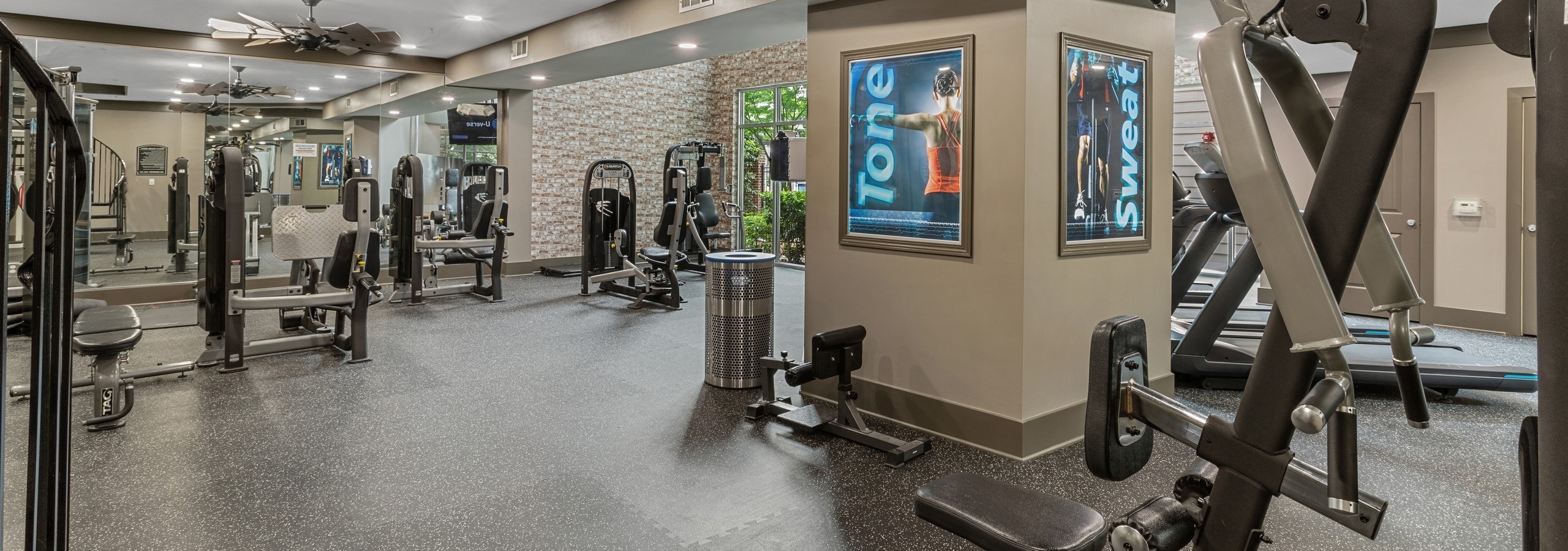 AMLI North Point fitness center with speckled floors and weight machines with ceiling fans and mirrored wall and windows