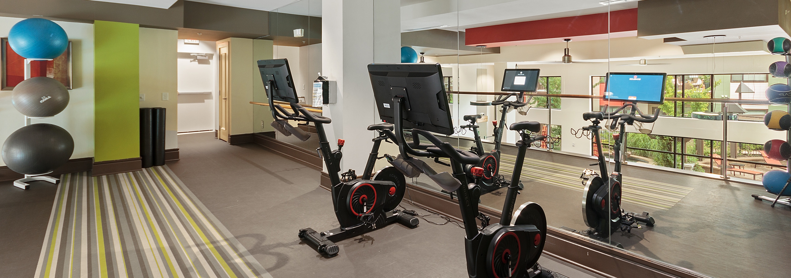 Upstairs interior of fitness center at AMLI Ponce Park with exercise bikes and medicine balls and floor to ceiling wall mirror