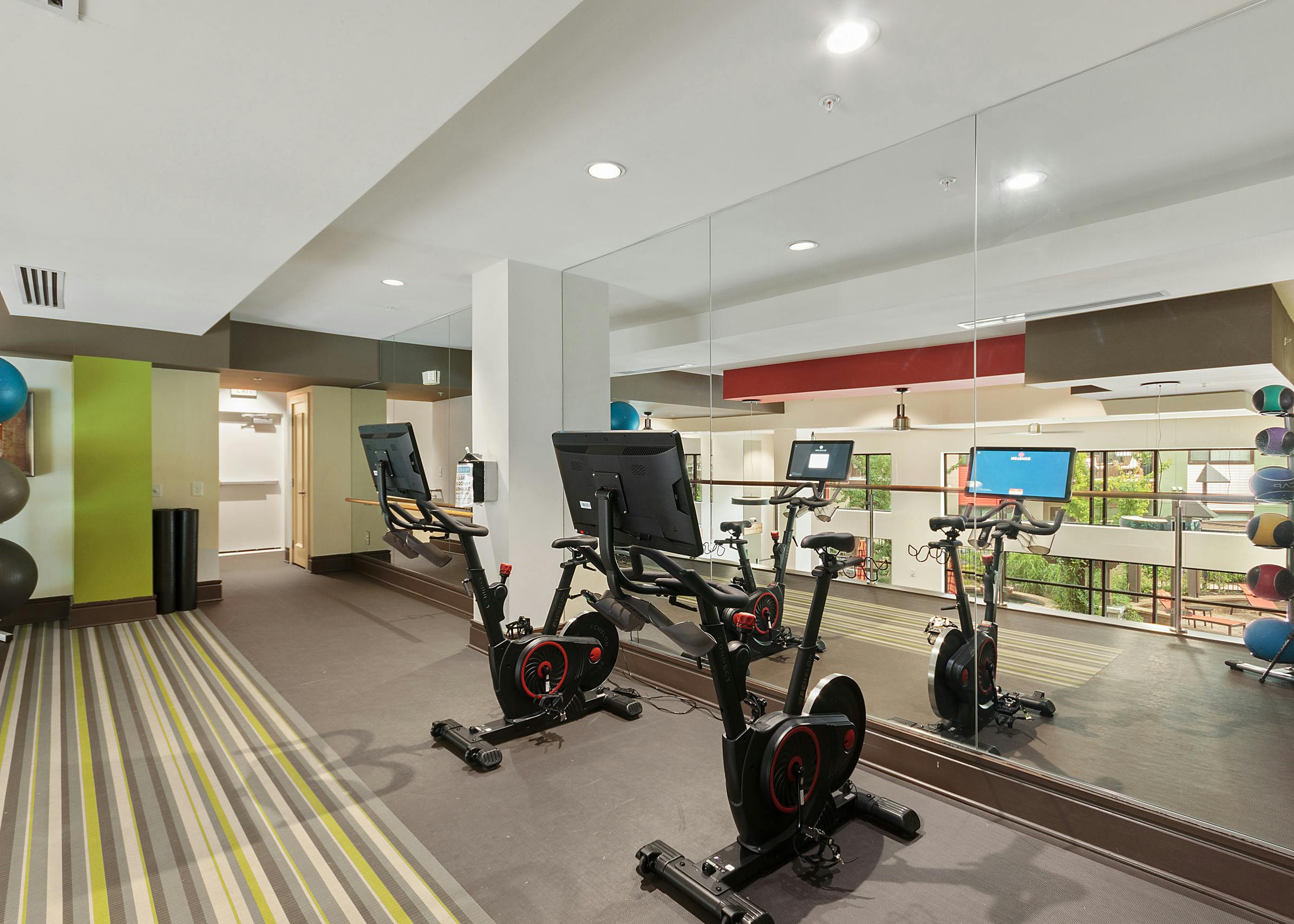 Upstairs interior of fitness center at AMLI Ponce Park with exercise bikes and medicine balls and floor to ceiling wall mirror