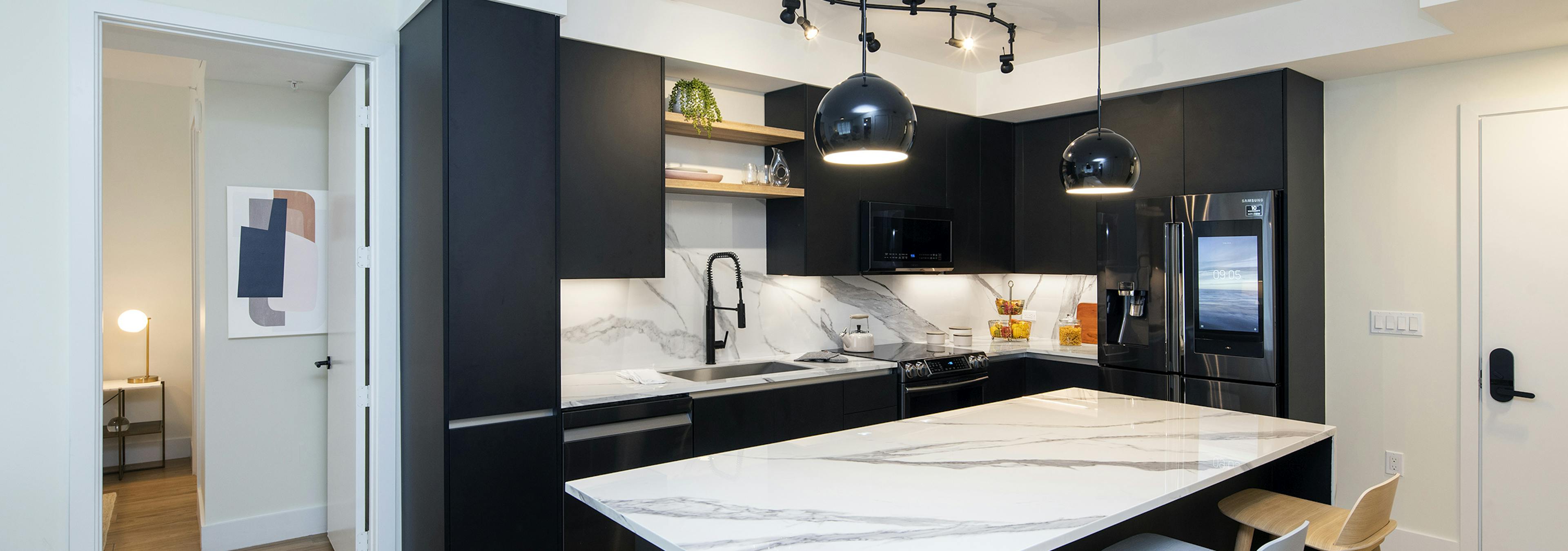 Interior of AMLI Midtown Miami apartment kitchen with marble island and three stools and dark cabinets and wood tile flooring