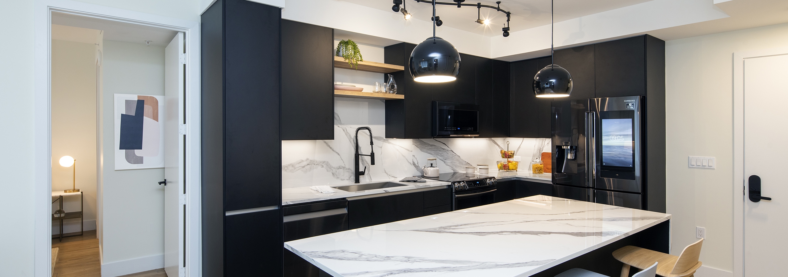 Interior of AMLI Midtown Miami apartment kitchen with marble island and three stools and dark cabinets and wood tile flooring