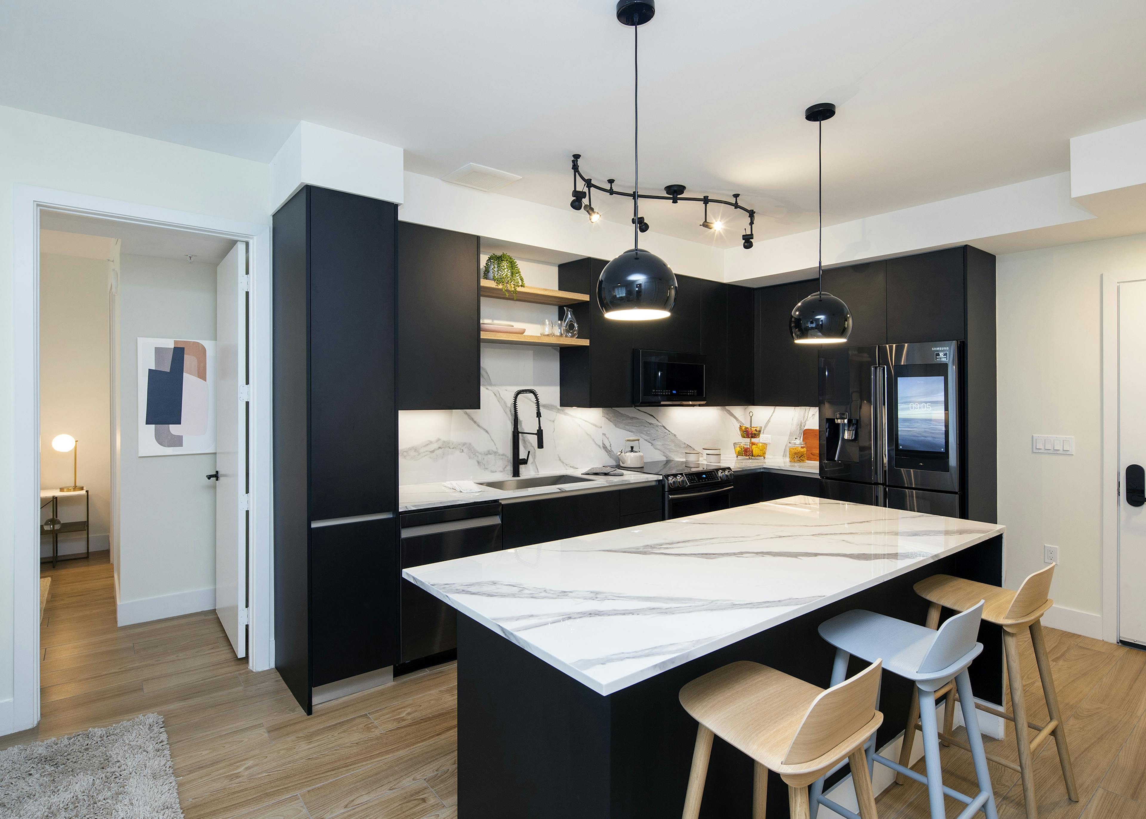 Interior of AMLI Midtown Miami apartment kitchen with marble island and three stools and dark cabinets and wood tile flooring