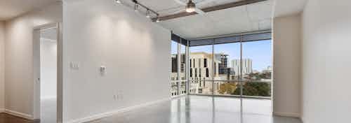 AMLI on 2nd living room with light walls and flooring with open door peeking into bedroom and floor to ceiling windows