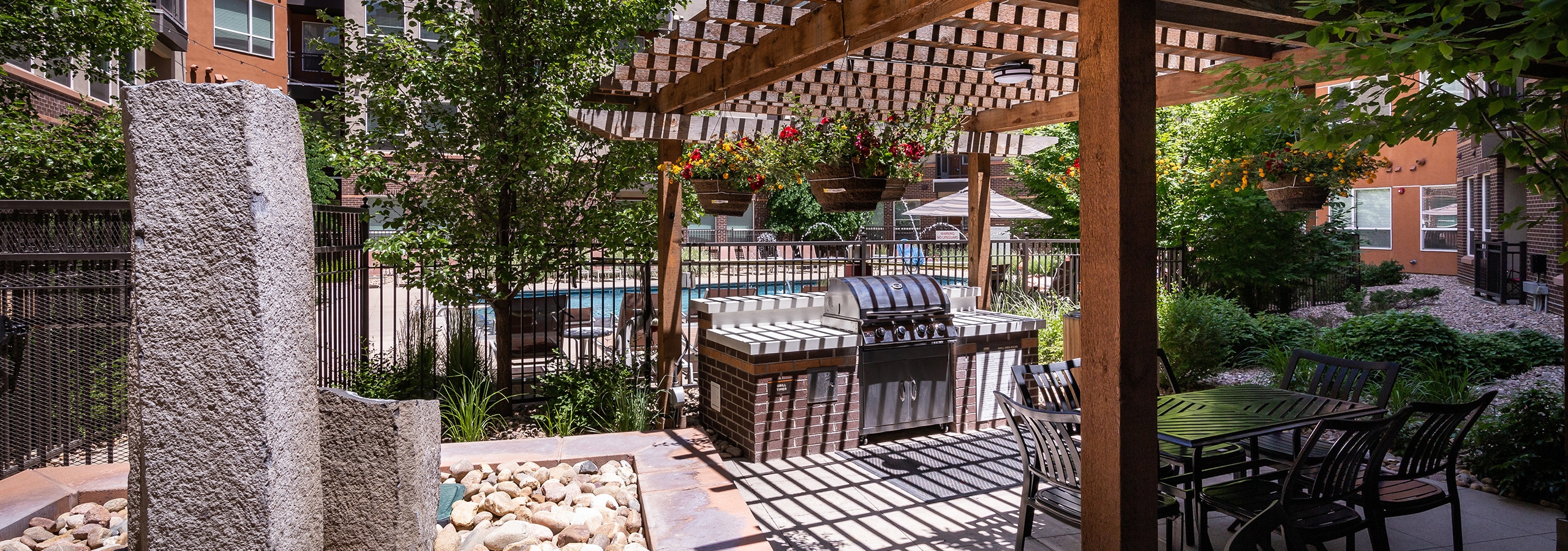 A barbecue area at AMLI Riverfront Park apartments with a wooden awning and a grill and tables and chairs and a fountain
