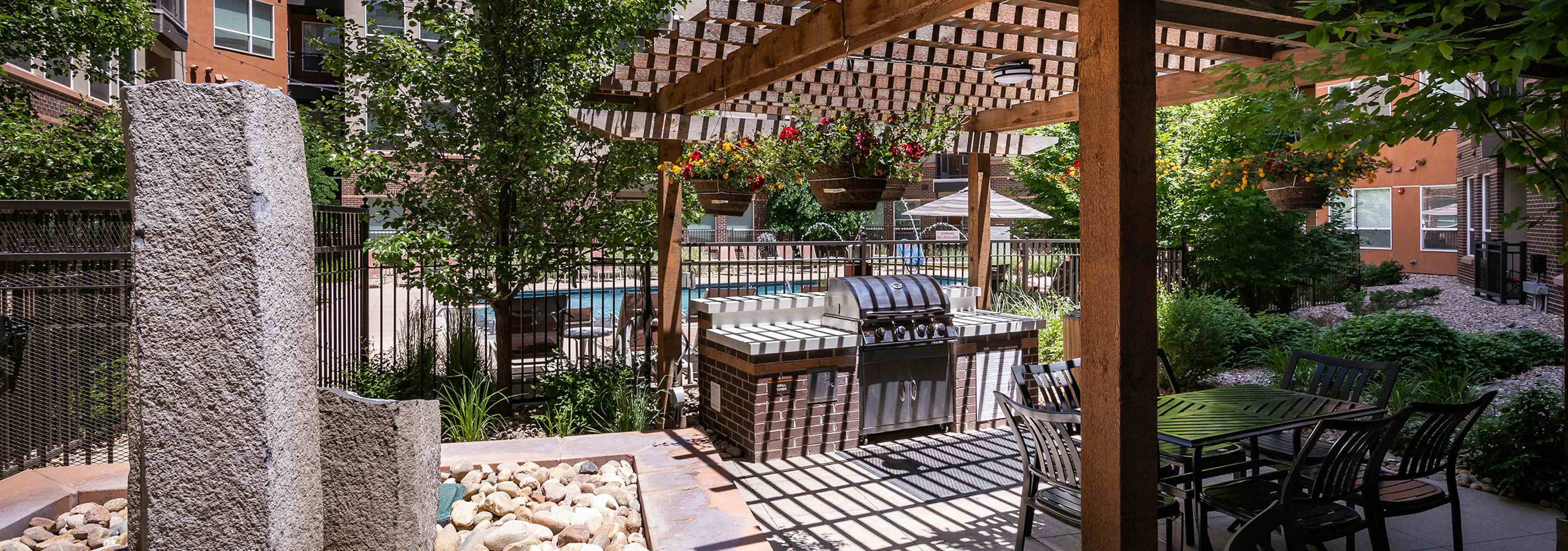 A barbecue area at AMLI Riverfront Park apartments with a wooden awning and a grill and tables and chairs and a fountain