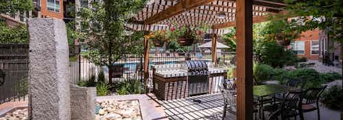 A barbecue area at AMLI Riverfront Park apartments with a wooden awning and a grill and tables and chairs and a fountain