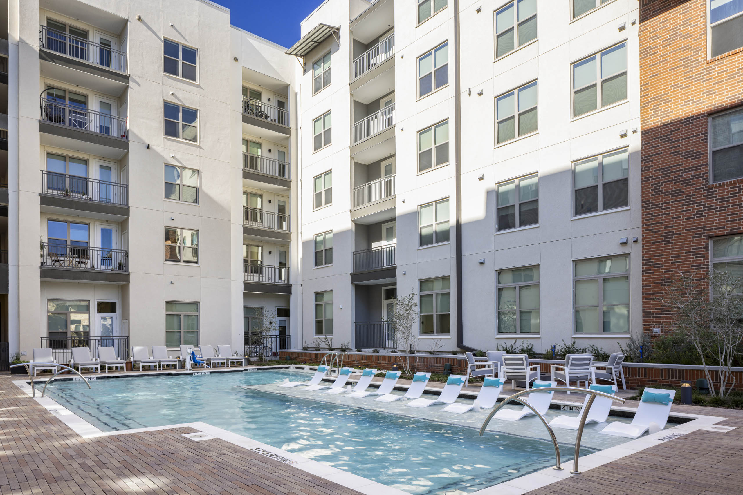 Daytime view of AMLI Branch Park apartments courtyard pool surrounded by white lounge chairs and green landscaping