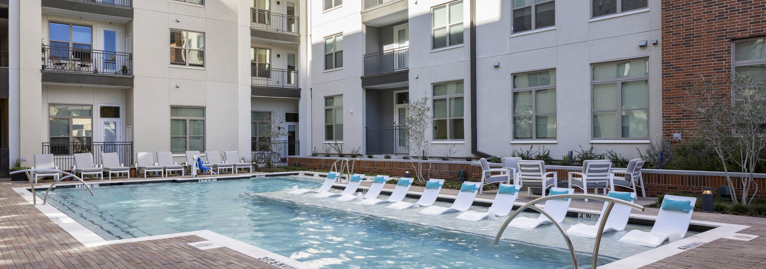 Daytime view of AMLI Branch Park apartments courtyard pool surrounded by white lounge chairs and green landscaping