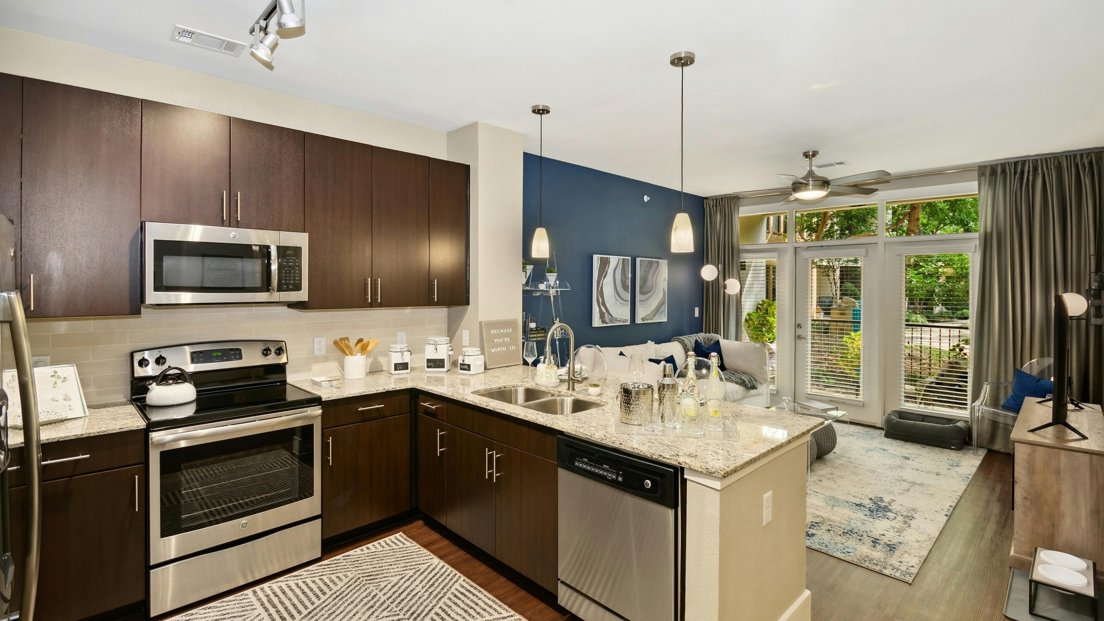 Interior of AMLI Campion Trail apartment kitchen with dark wood cabinets and stainless steel appliances and living room