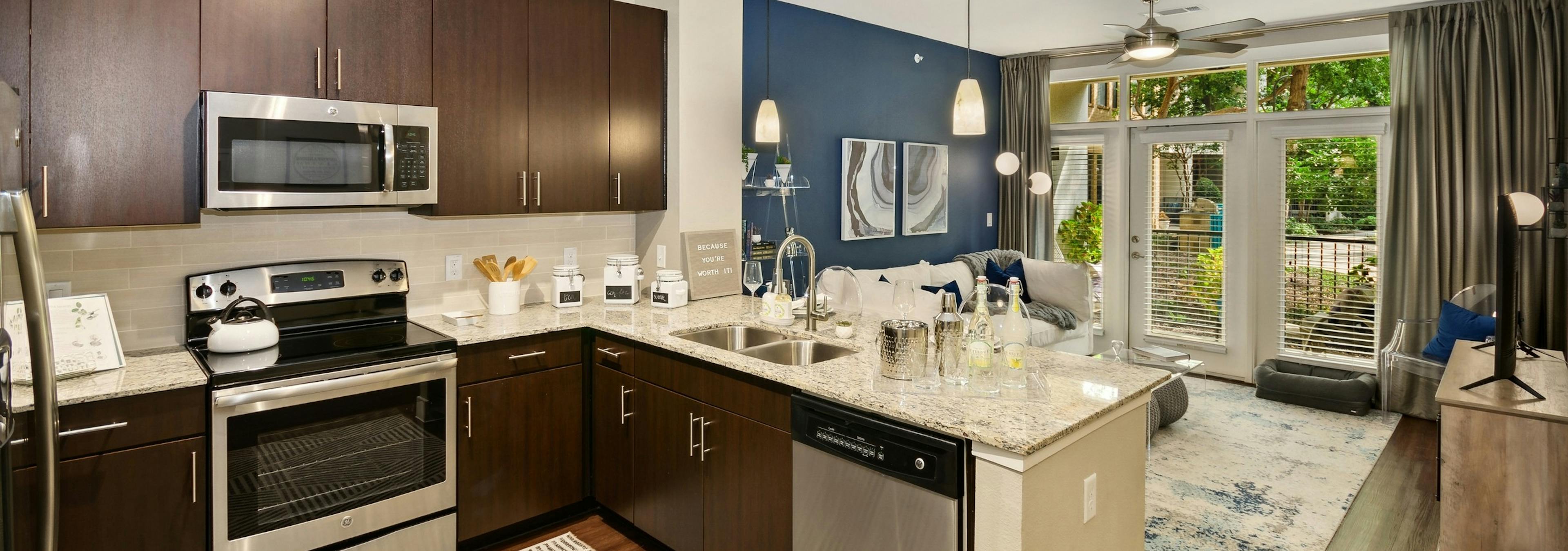 Interior of AMLI Campion Trail apartment kitchen with dark wood cabinets and stainless steel appliances and living room