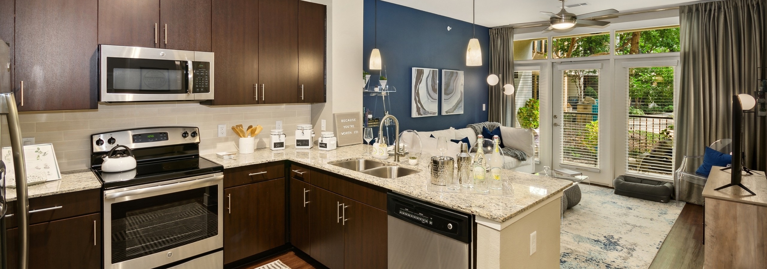 Interior of AMLI Campion Trail apartment kitchen with dark wood cabinets and stainless steel appliances and living room