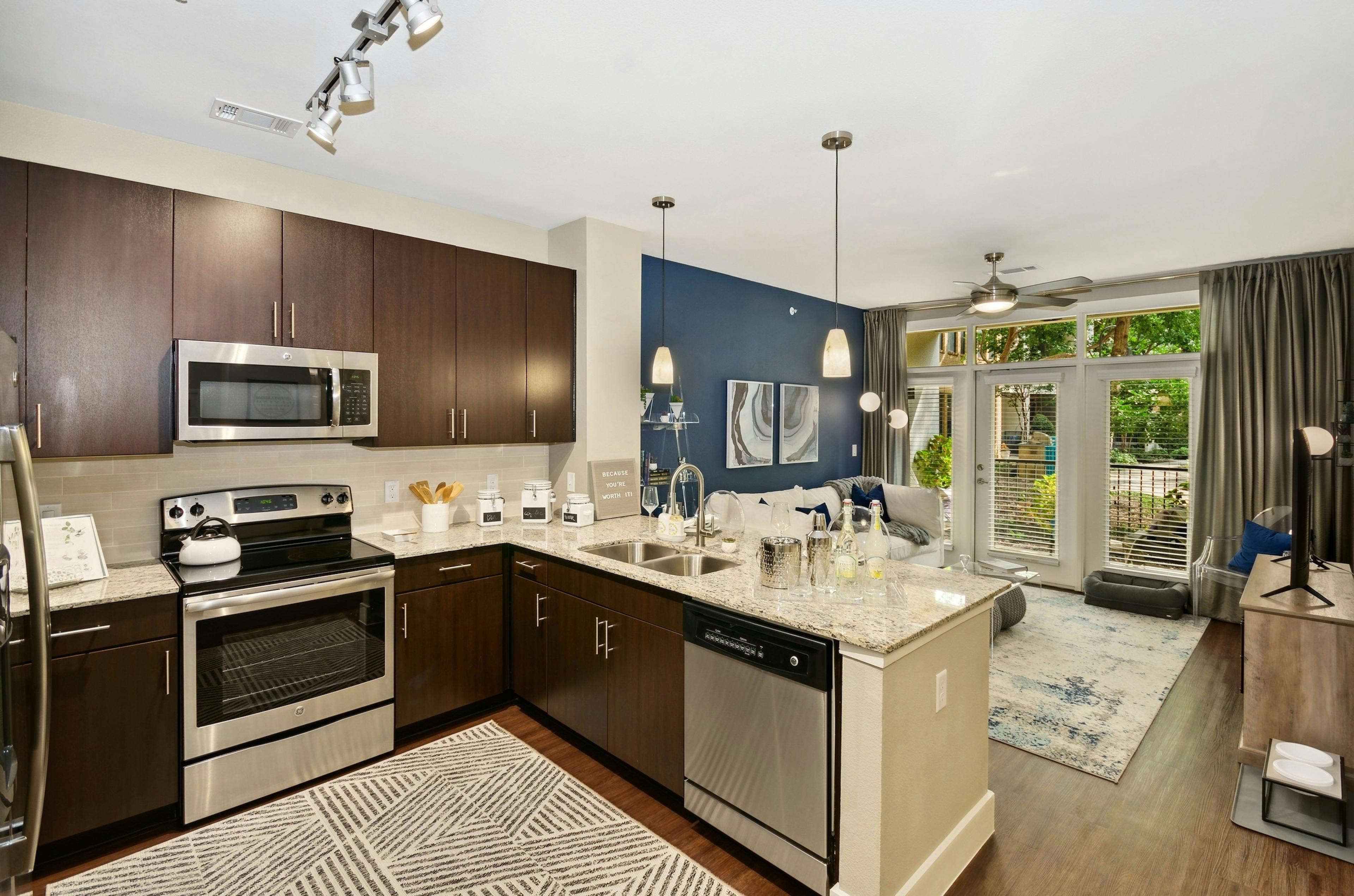 Interior of AMLI Campion Trail apartment kitchen with dark wood cabinets and stainless steel appliances and living room