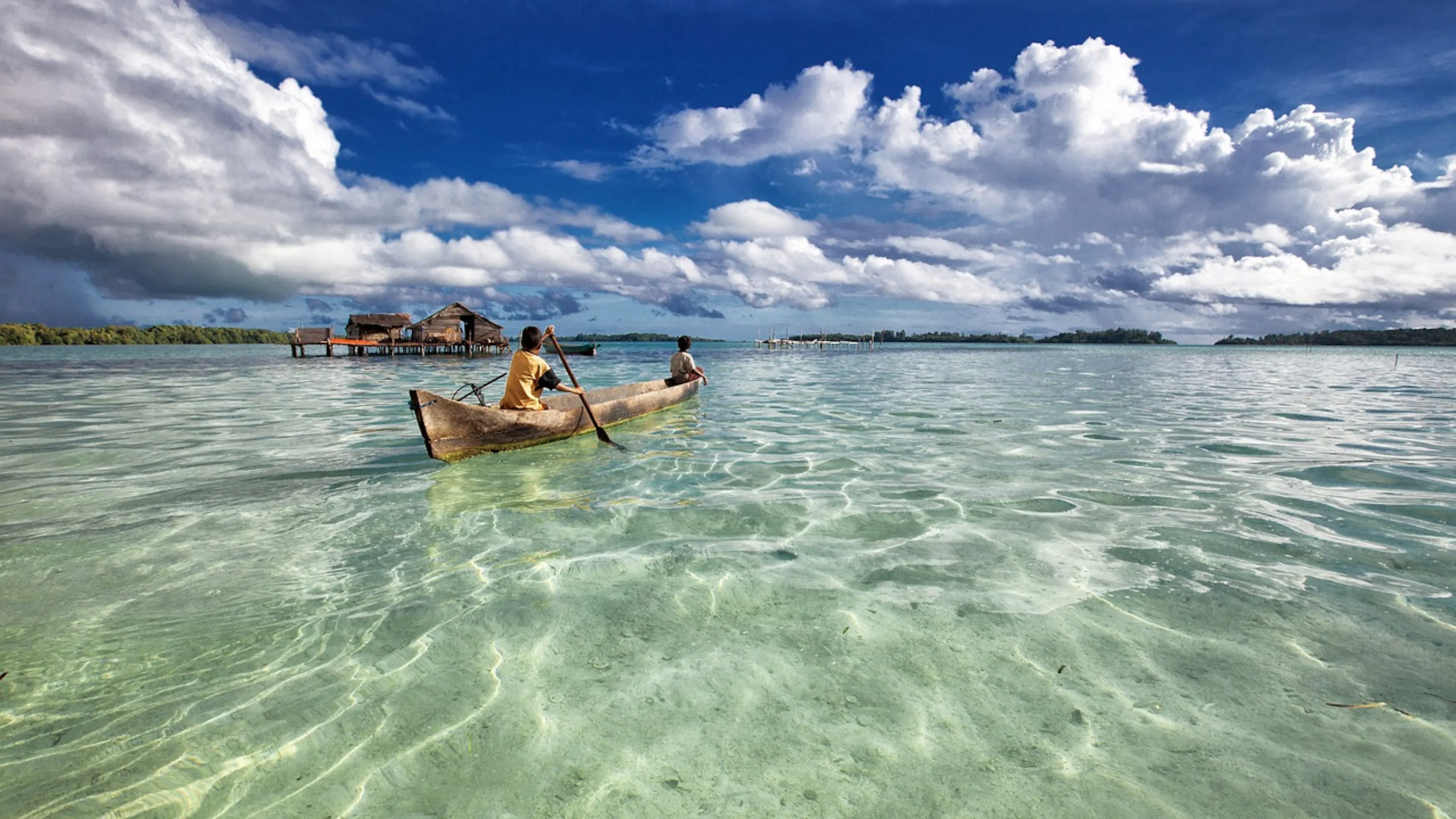 Two children on an Indonesian canoe on a shallow shoal on a clear and sunny day