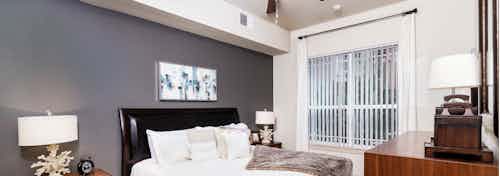 Interior view of a bedroom at AMLI Park Avenue apartments with a bed with black head board and lamps with glass balcony door