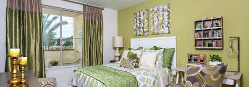 Interior view of AMLI Spanish Hills bedroom with queen bed and white headboard facing large window with green satin curtains