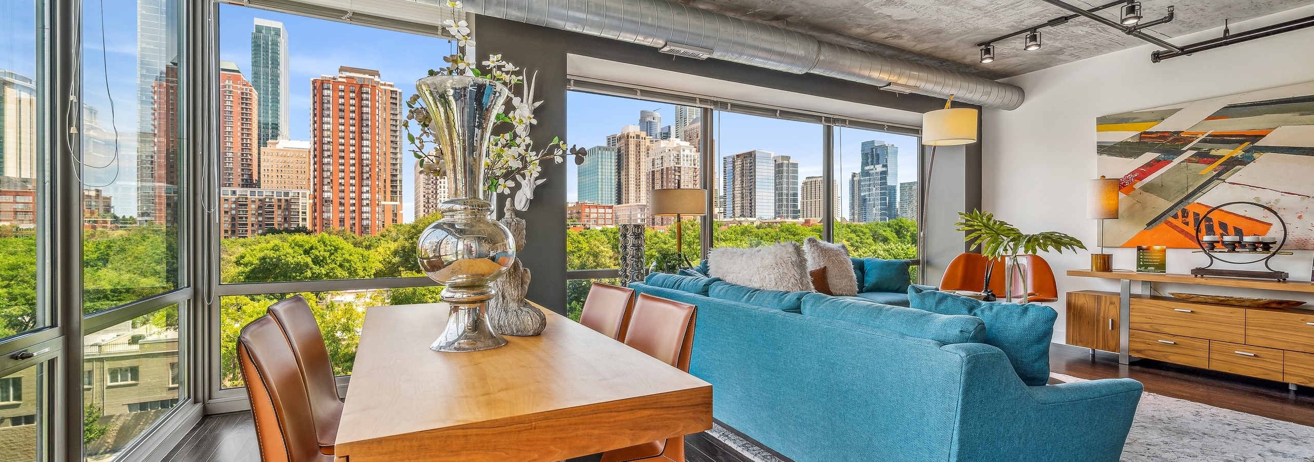 AMLI 900 dining and living room with beautiful view of city and wood table and 4 leather chairs with artwork and blue couches