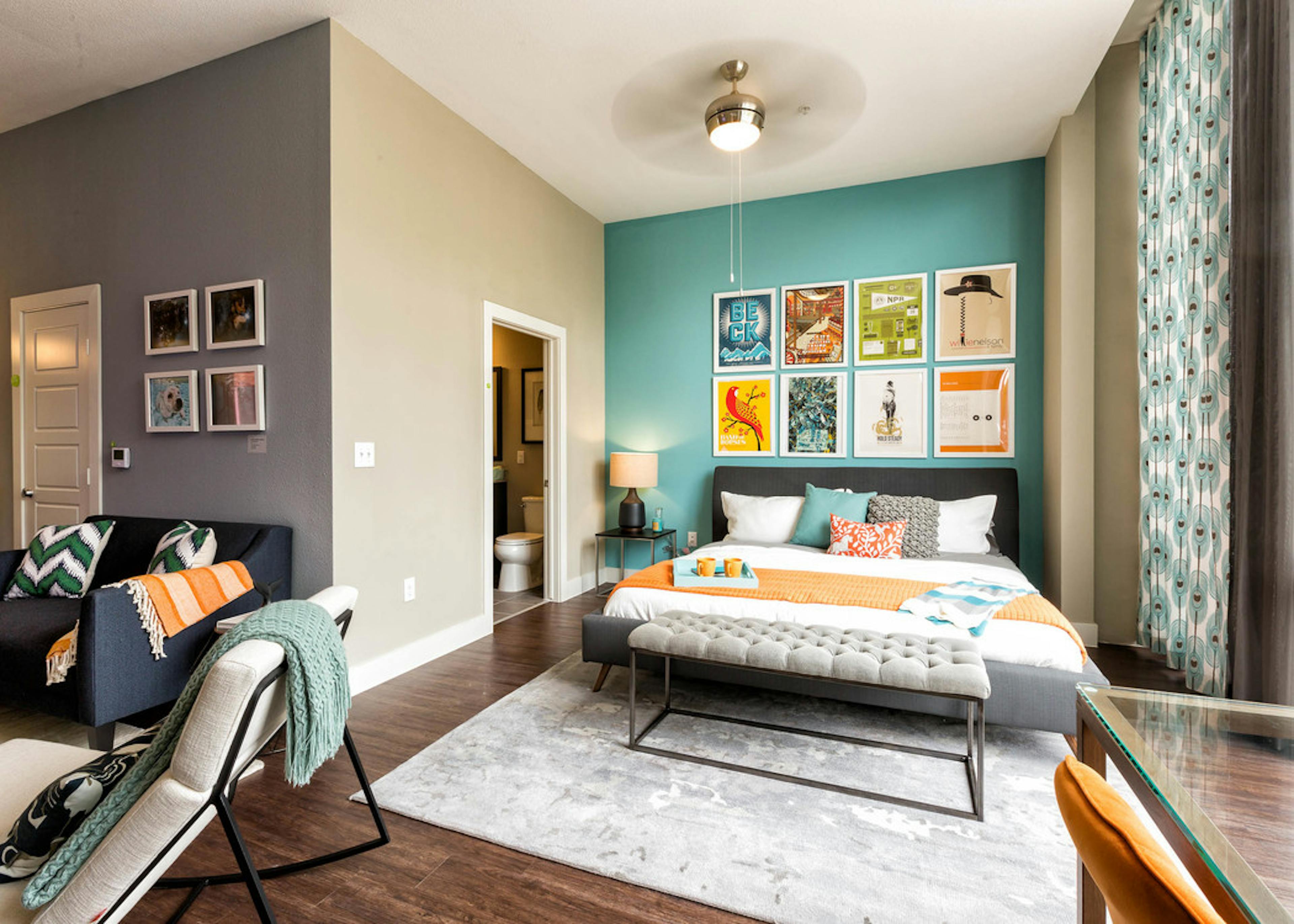 AMLI at Mueller bedroom with a teal accent wall and colorful wall art hanging above bed with peek into connecting bathroom