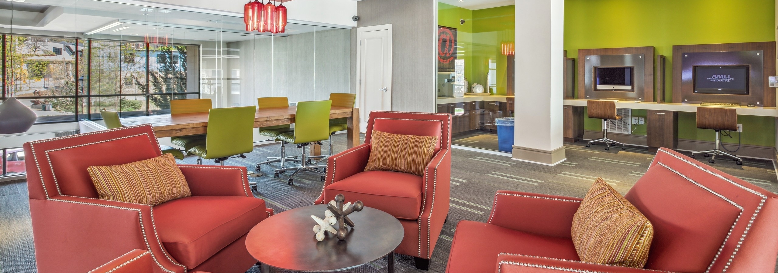 Colorful interior view of AMLI Ponce Park business center with computer stations and 4 orange chairs for resident gatherings