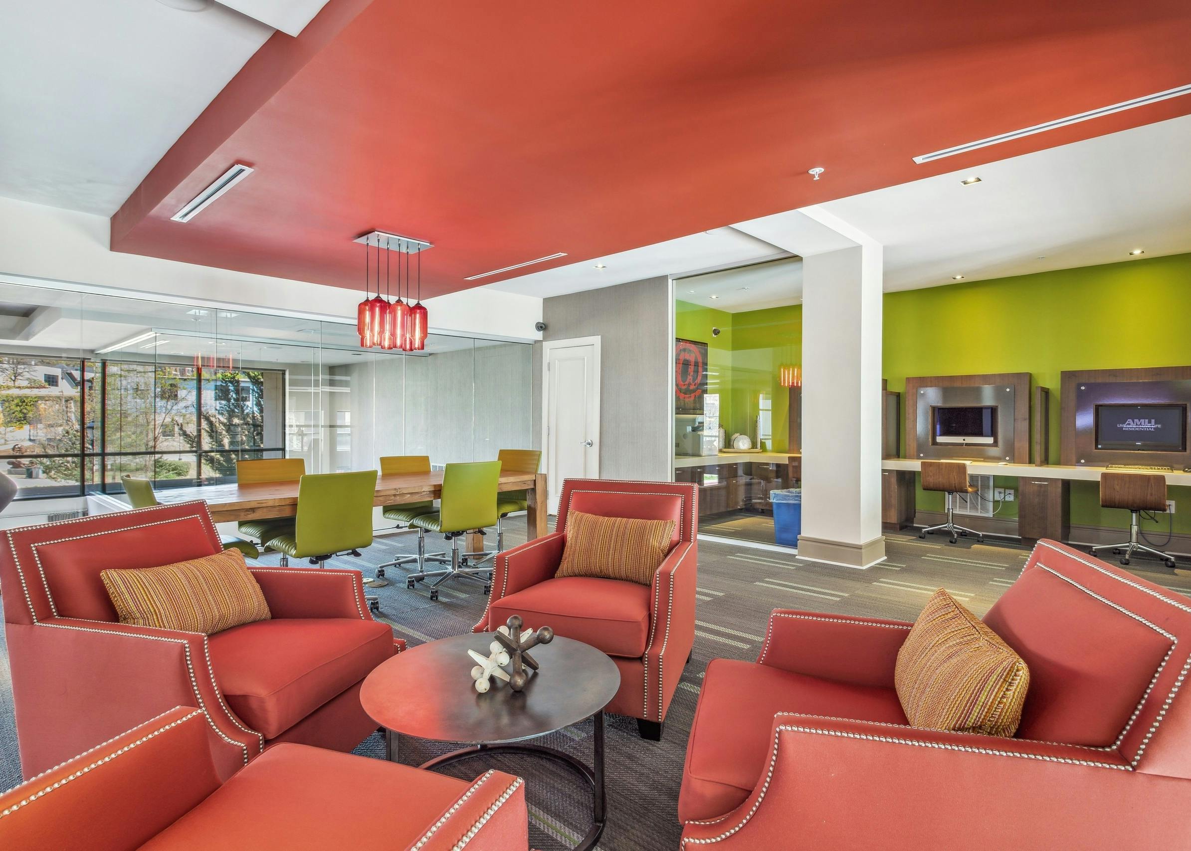 Colorful interior view of AMLI Ponce Park business center with computer stations and 4 orange chairs for resident gatherings