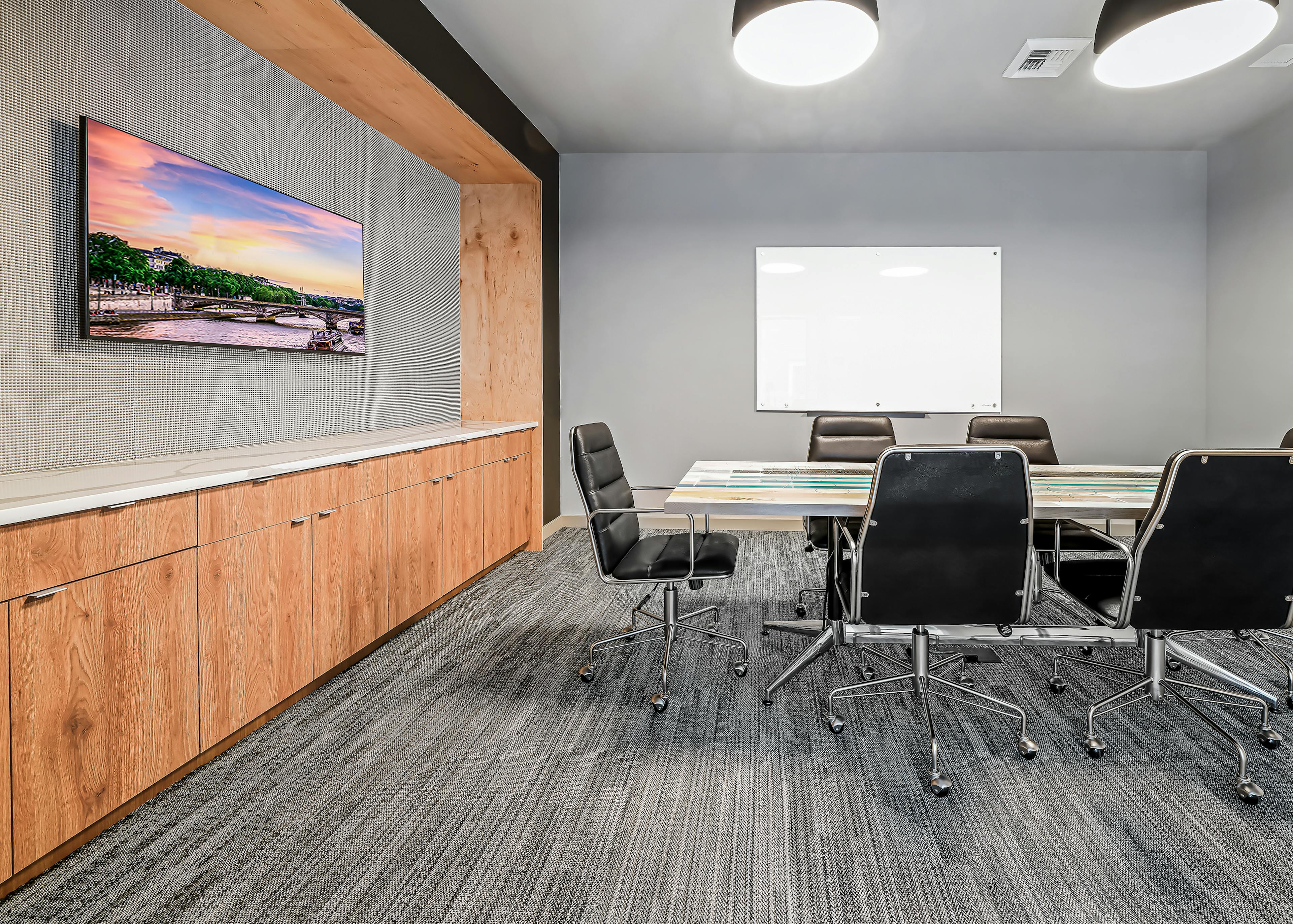 Conference room at AMLI Spring District with white table and 6 black chairs and whiteboard and mounted TV over wood cabinets