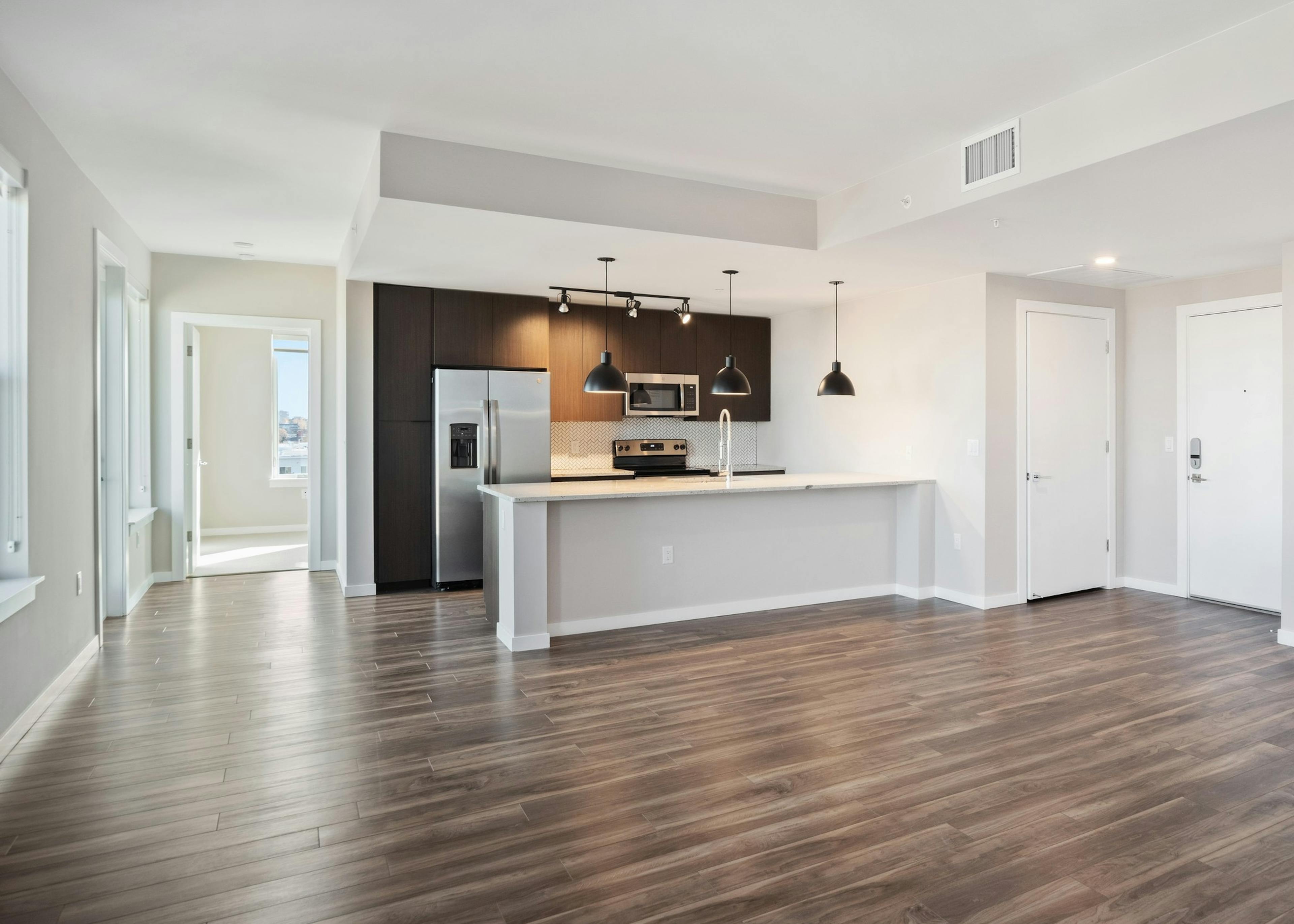AMLI at Uptown open apartment living area with view of modern kitchen featuring dark cabinetry and modern light fixtures