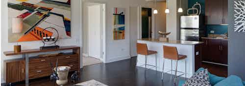 Modern kitchen and living room at AMLI 900 where colorful art hangs on the walls paired with dark wood cabinets and flooring