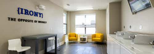 Interior of laundry room at AMLI West Plano with washer and dryer machines and dark hardwood with yellow and white seating