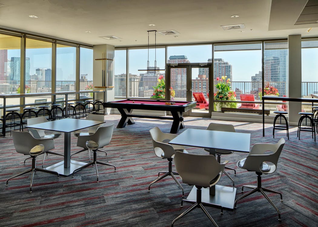 Rooftop lounge at AMLI 900 featuring tables, chairs and a pool table surrounded by glass windows with a daytime city view
