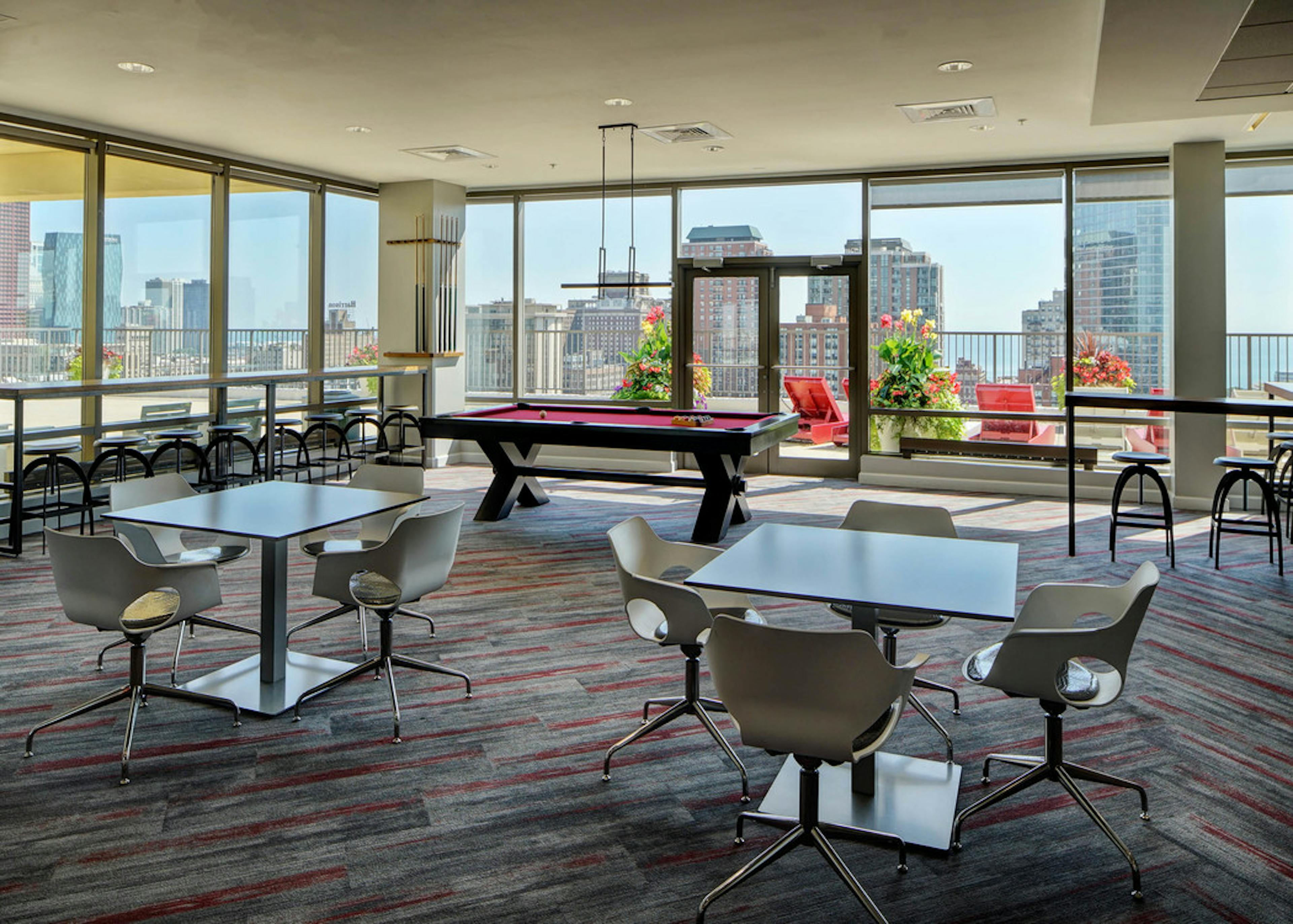 Rooftop lounge at AMLI 900 featuring tables, chairs and a pool table surrounded by glass windows with a daytime city view