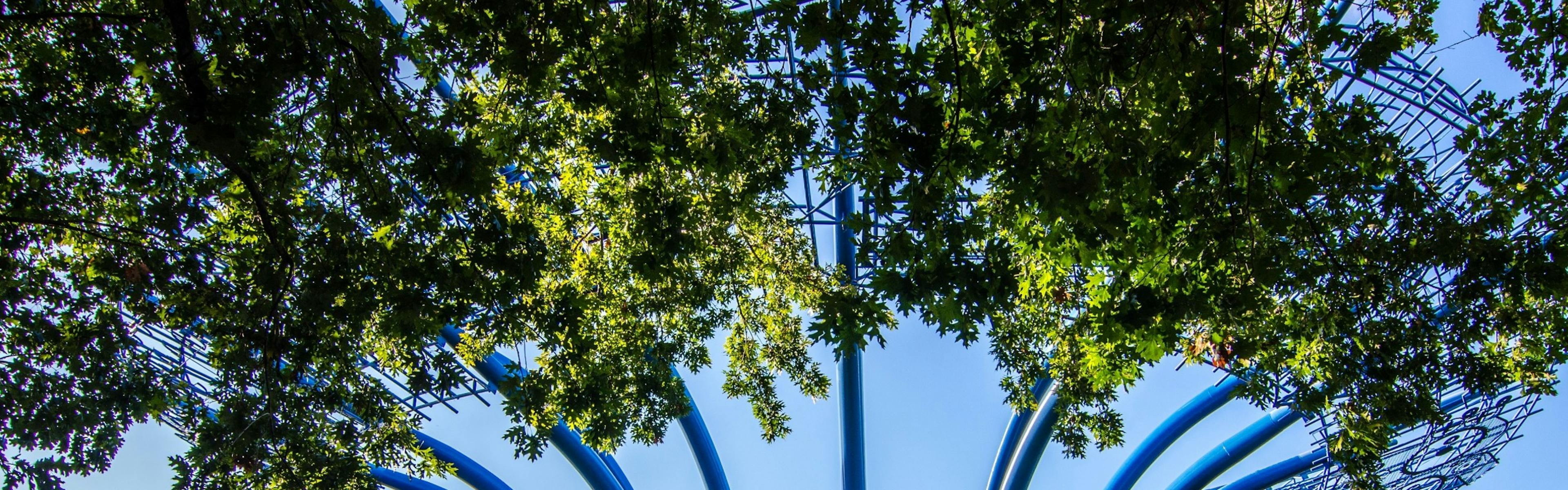 Close up view from beneath the Blueprints at Addison steel art structure with bright blue sky and tree leaves near the camera